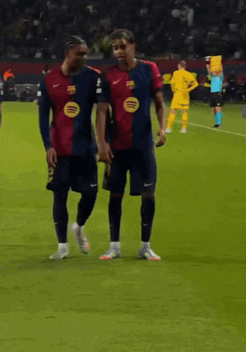 two soccer players are walking on the field and one has a spotify logo on his jersey