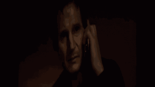 a man in a black shirt is talking on a cell phone in a dark room .