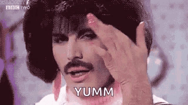 a man with a mustache is making a funny face with his hand on his forehead .