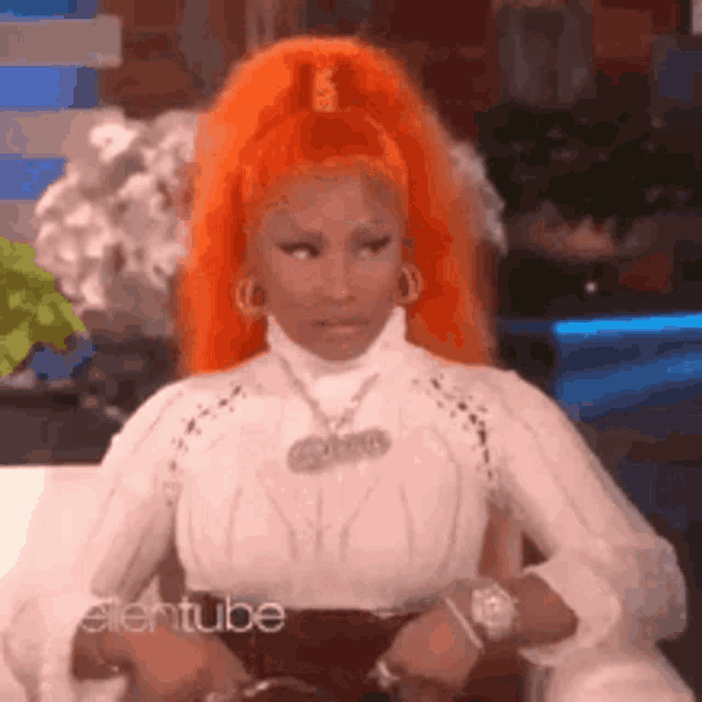 a woman with orange hair is sitting on a couch wearing a white shirt .