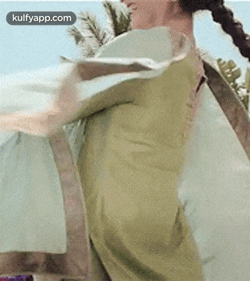 a woman in a green dress is standing on a beach with her arms outstretched and her hair in a braid .