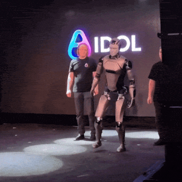 a man in a black shirt stands next to a robot in front of an idol sign