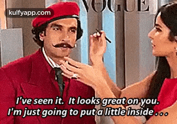 a woman is applying makeup to a man 's face in a red suit and hat .