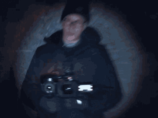 a man wearing glasses and a beanie holds a camera