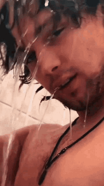 a shirtless man is taking a shower and water is coming out of his mouth