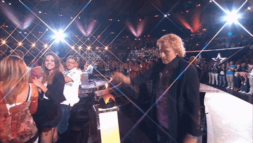a man stands on a stage in front of a crowd wearing a shirt that says fly emirates on it