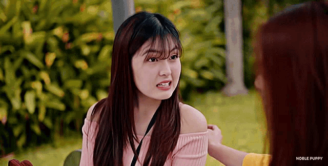 a girl in a pink off the shoulder top is talking to another girl in a park .