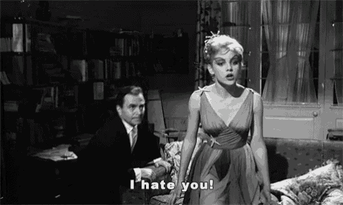 a woman in a dress is standing in front of a man in a suit and tie and saying i hate you .
