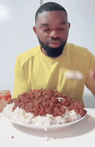 a man in a yellow shirt is eating a plate of rice and beans