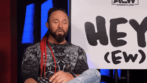 a man sitting in front of a sign that says hey ew