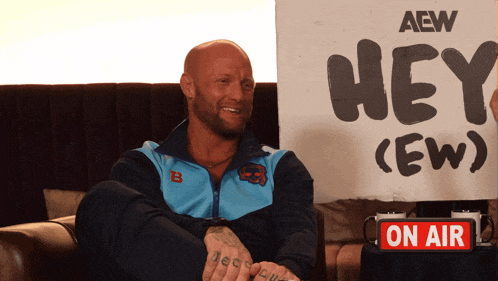 a man sitting on a couch holding a sign that says hey crew