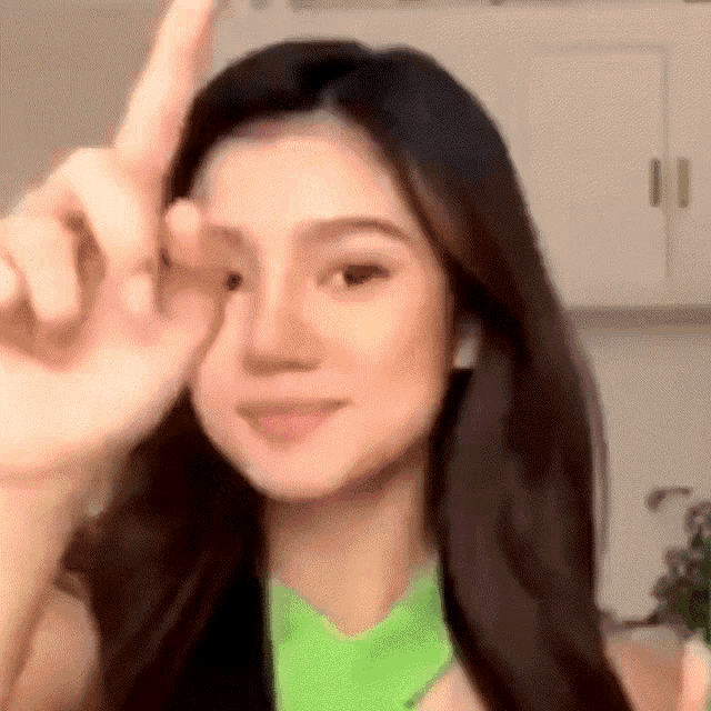 a woman in a green tank top is making a peace sign with her hand .