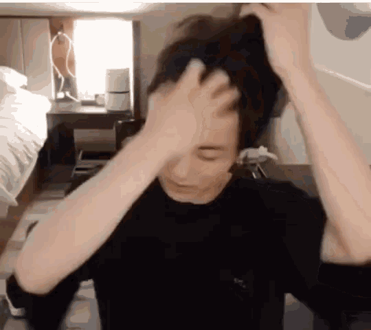 a man in a black shirt is scratching his head with his hand .