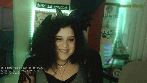 a woman wearing a bat headband is smiling in front of a happy halloween sign