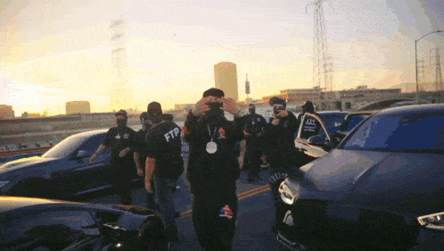 a man wearing a ftp sweatshirt stands in front of a group of cars