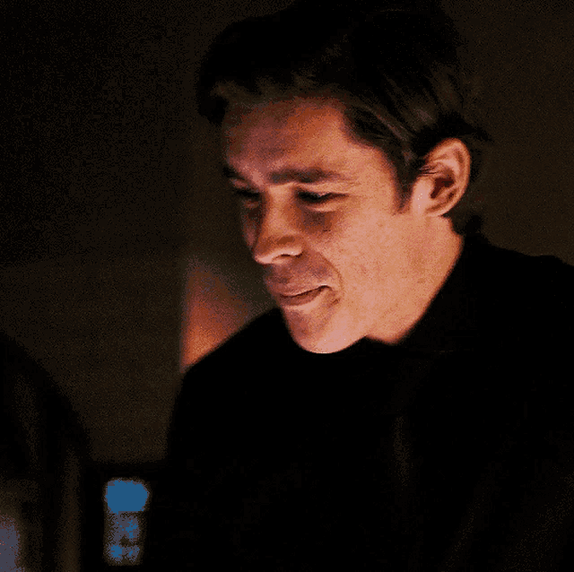 a man in a black shirt and tie is smiling in the dark