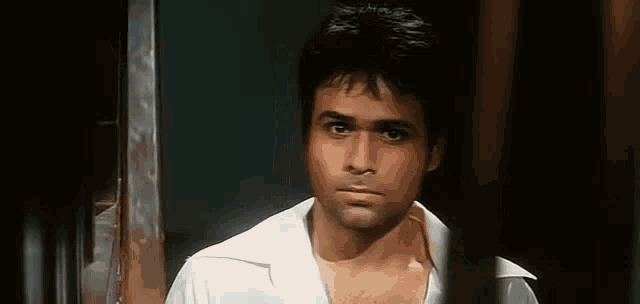 a man in a white shirt is standing in a dark room behind a fence .