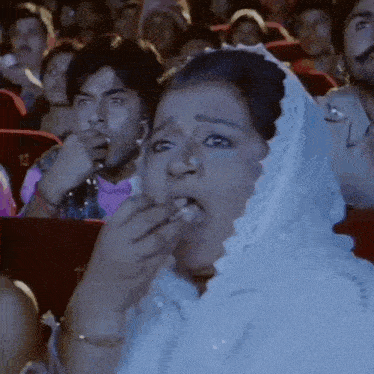 a woman in a white veil is eating a piece of food while watching a movie