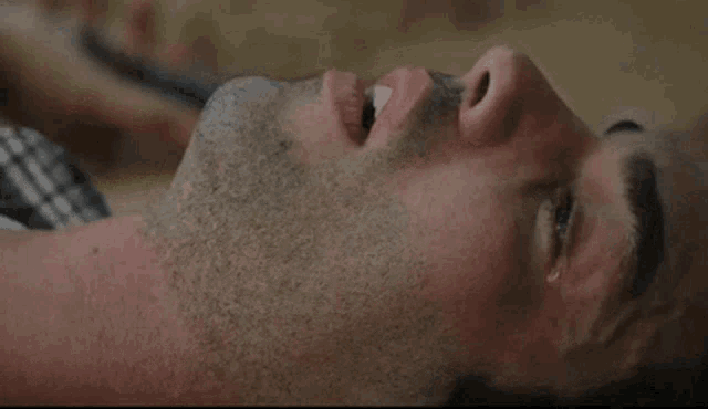 a man with a beard is laying on the ground with his eyes closed and his mouth open .