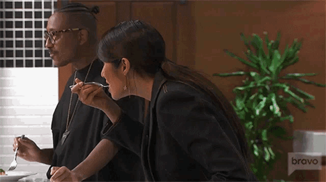 a man and a woman are sitting at a table eating food with bravo on the bottom right