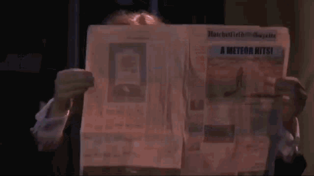 a person is holding a newspaper in front of their face in a dark room .