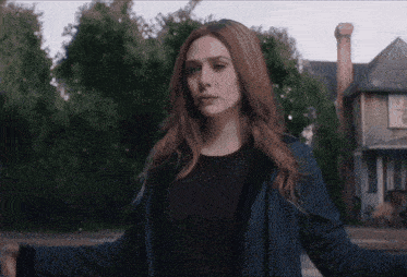 a woman with red hair stands in front of a house with her arms outstretched