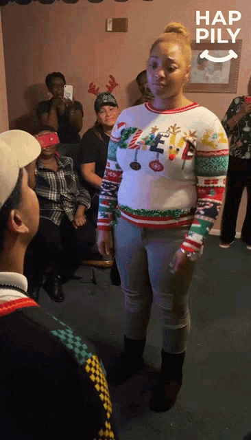 a woman wearing an ugly christmas sweater stands in front of a group of people with hap pily written on the bottom