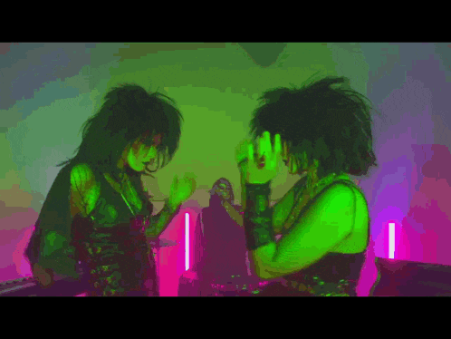 two women are standing next to each other in a room with green lights