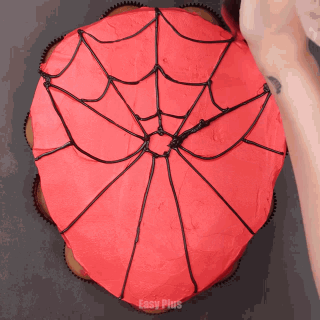 a spiderman cupcake with red frosting and a black spider web