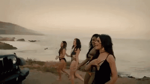 a group of women in swimsuits are running towards the ocean next to a jeep .