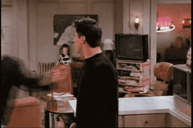 a man in a black shirt is standing in a living room in front of a tv .