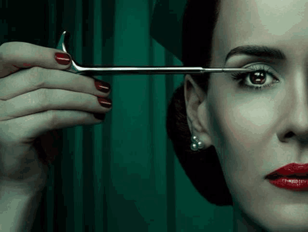 a woman with red nails is holding a pair of scissors over her eye .