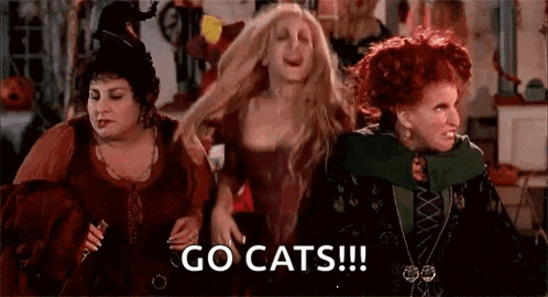 three witches are dancing in a room with the words `` go cats '' written on the bottom .