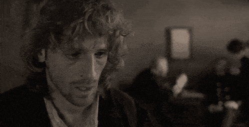 a man with curly hair and a beard is sitting in a dark room