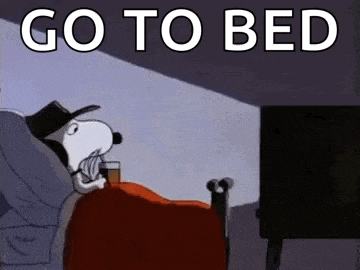 snoopy is laying in bed with a glass of whiskey and watching tv .
