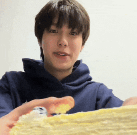 a man in a blue hoodie is holding a piece of cake in his hand