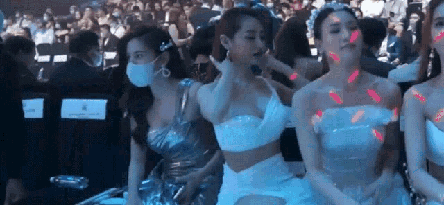 a group of women are sitting in a stadium wearing masks and dresses .