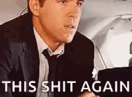 a man in a suit and tie is smoking a cigarette while sitting in a car with the words `` this shit again '' .