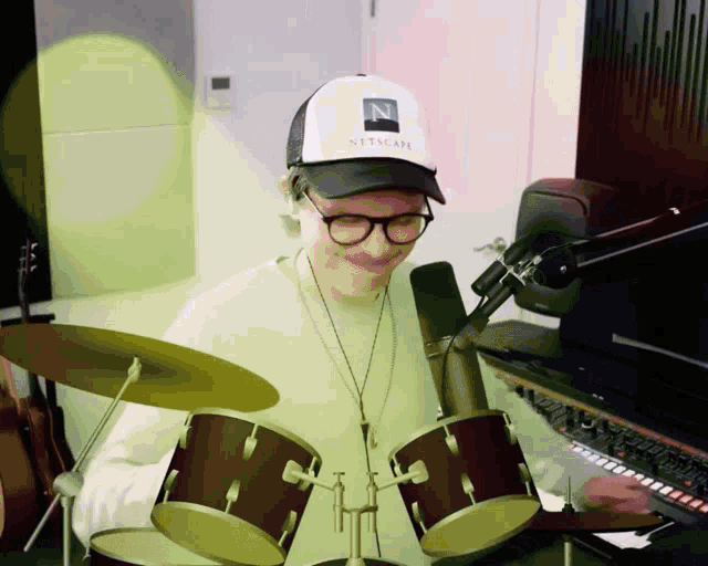 a man wearing a netscape hat is playing a drum set