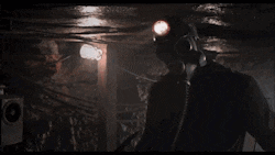 a man wearing a gas mask and a helmet is standing in a dark room .