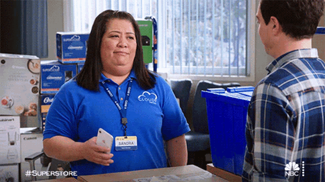 a woman wearing a blue shirt that says sandra is talking to a man in a plaid shirt