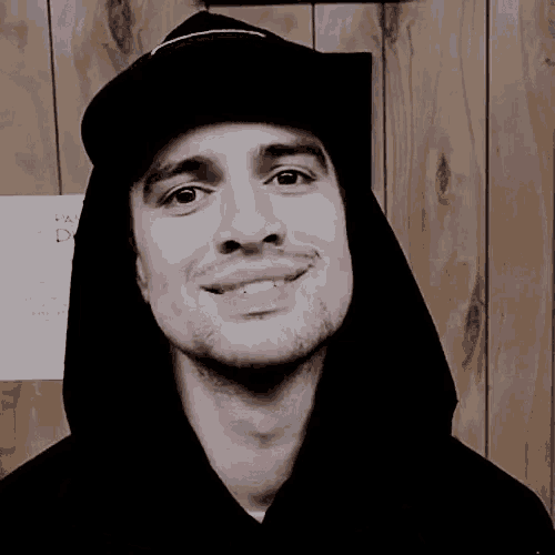 a man wearing a hooded sweatshirt and a hat smiles for the camera