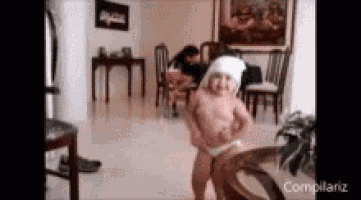 a baby in a diaper is dancing in a living room with a woman sitting in the background .