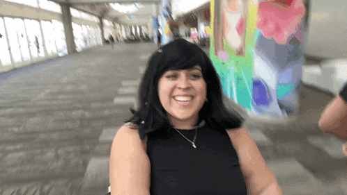a woman wearing a black top and a necklace smiles