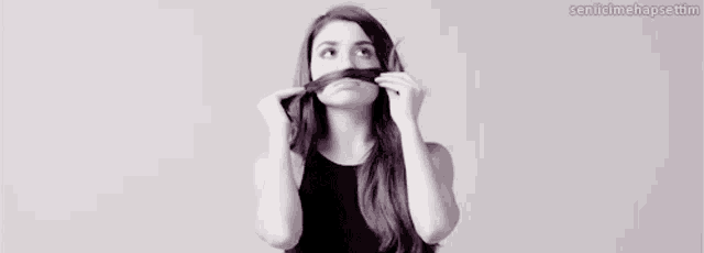 a black and white photo of a woman holding her hair in front of her mouth .
