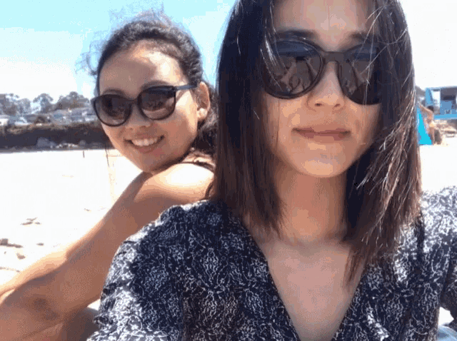 two women wearing sunglasses pose for a picture on a beach