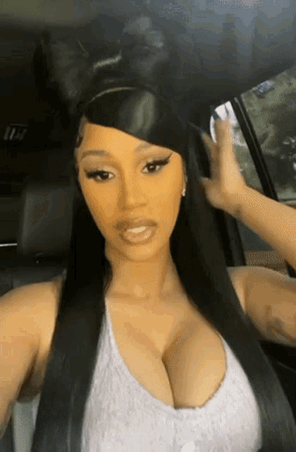 cardi b is taking a selfie in the back seat of a car while wearing bunny ears .
