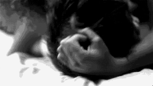a black and white photo of a couple laying on a bed holding each other 's faces .