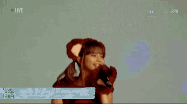 a woman in a bear costume singing into a microphone with the words kebun binatang di saat hujan on the bottom