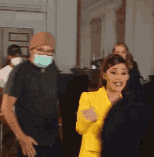 a man wearing a mask is standing next to a woman in a yellow jacket
